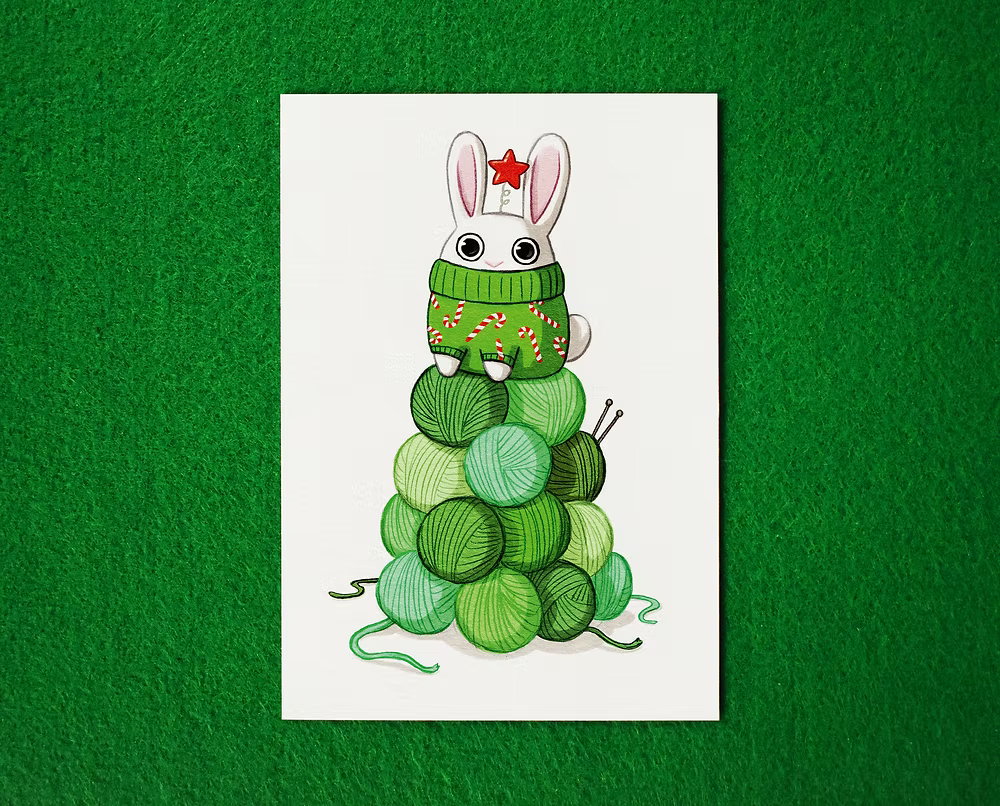 Illustration of a bunny in a green sweater with candy can sitting on stacked green yarn balls, to look liek a Christmas Tree. Bunny has a little red star headband.