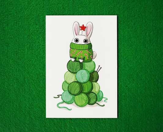 Illustration of a bunny in a green sweater with candy can sitting on stacked green yarn balls, to look liek a Christmas Tree. Bunny has a little red star headband.  