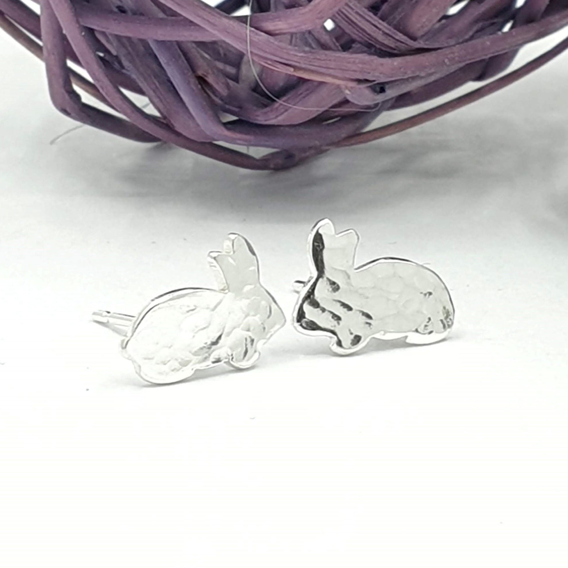 Silver earrings of a sideways facing rabbit with a hammered texture