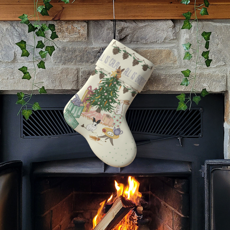 A cream coloured Christmas stocking hung from a mantlepiece. on the stocking is a festive, hand drawn image of 4 playful bunnies causing mischief around a Christmas tree, under the phrase 'all is calm, all is bright'.