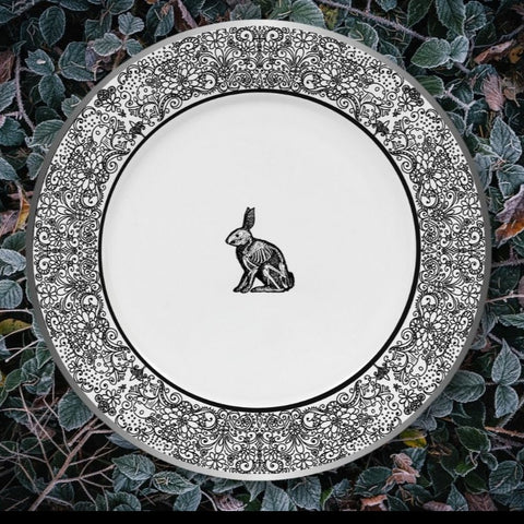 gothic dinner plate. a black bunny rabbit silhouette with the skeletons visible, on a white background, the rim is covered in a field of elaborate, black, floral swirls on a white background.