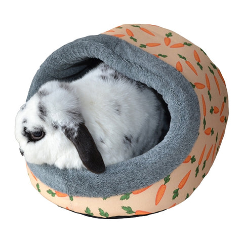 White and black fluffy lop bunny peeks out of a Rosewood plush rabbit bed with carrot pattern.